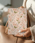 A5 grandmacore journal with a blush-pink cover, dense peach and blush blossoms, and sage-green leaves